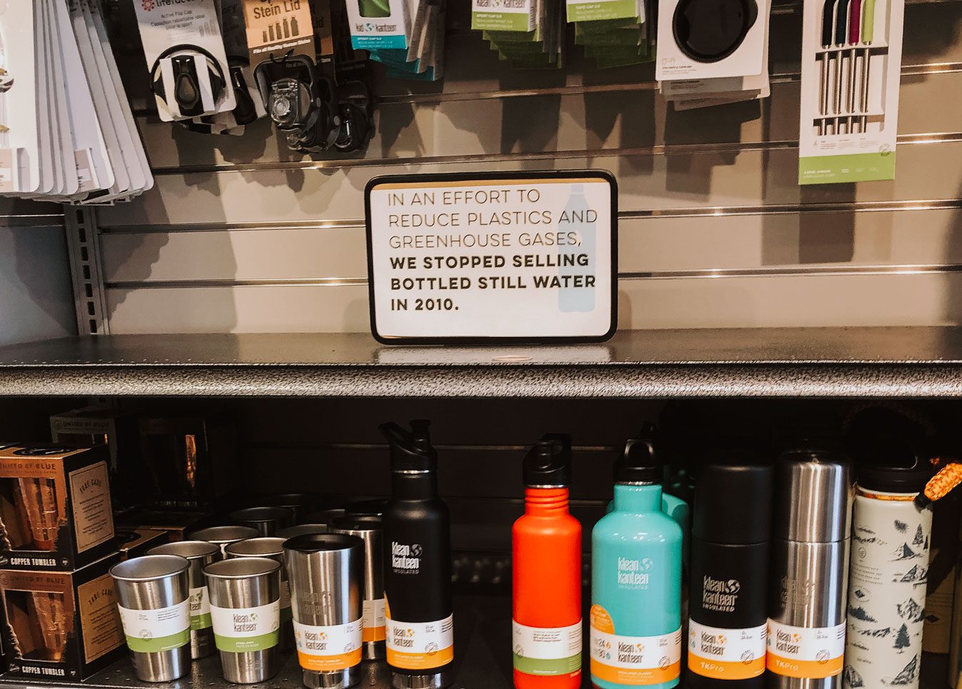 MOM's water bottle set with a sign that says "In an effort to reduce plastics and greenhouse gases we stopped selling bottled still water in 2010."